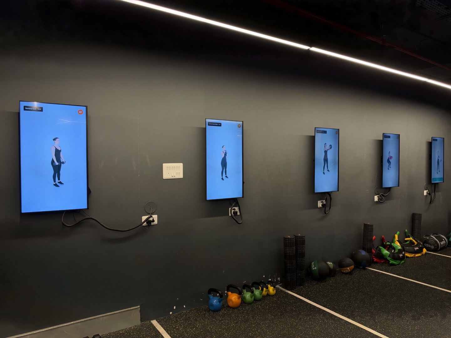 Multiple portrait screens showing exercise videos across a gym training area